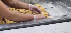 Baker wearing gloves arranges small dough rolls on a cooling rack in a bakery.