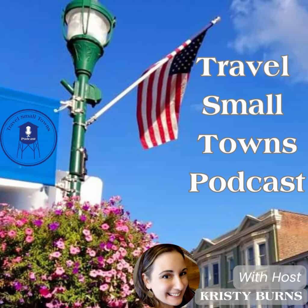 Cover image for the Travel Small Towns Podcast featuring a blue sky, a green streetlamp, an American flag, pink flowers, and a circular podcast logo with a microphone; shows host portraits overlapping the right side.