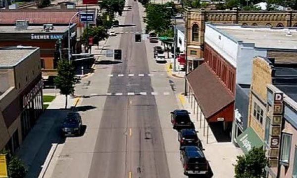 Bird's-eye view of a small town main street with storefronts, parked cars, and light traffic on both sides.